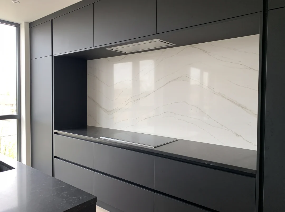 Minimalist charcoal kitchen with a continuous quartz slab backsplash behind the cooktop