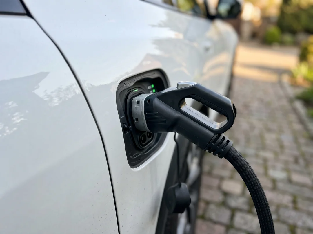 Connecteur de recharge branché dans le port de charge d'un véhicule électrique blanc, entrée résidentielle en arrière-plan.