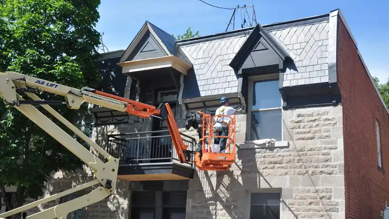Un membre de l'équipe travaille la façade depuis une nacelle, au niveau de la corniche