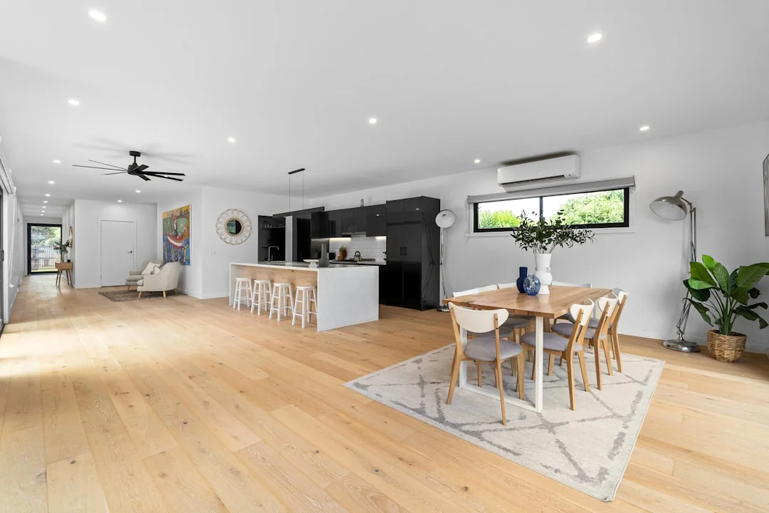 Large open-plan renovated space with light wood floors, black kitchen island and bright dining area