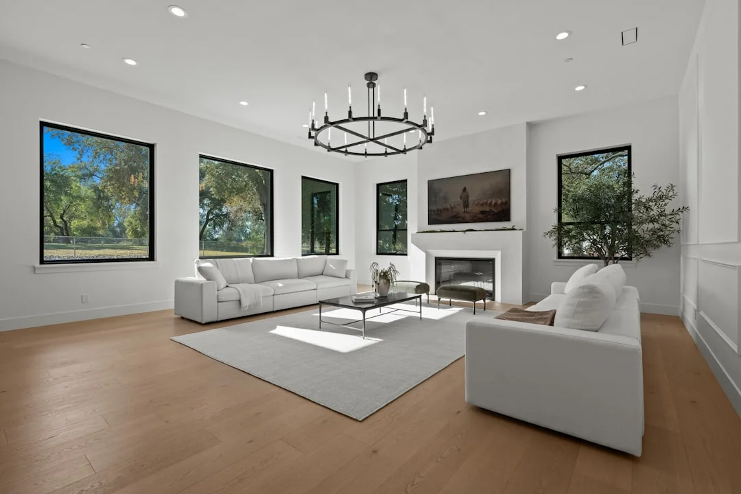 Large bright modern living room with warm medium-brown oak hardwood floor, white sofas and fireplace