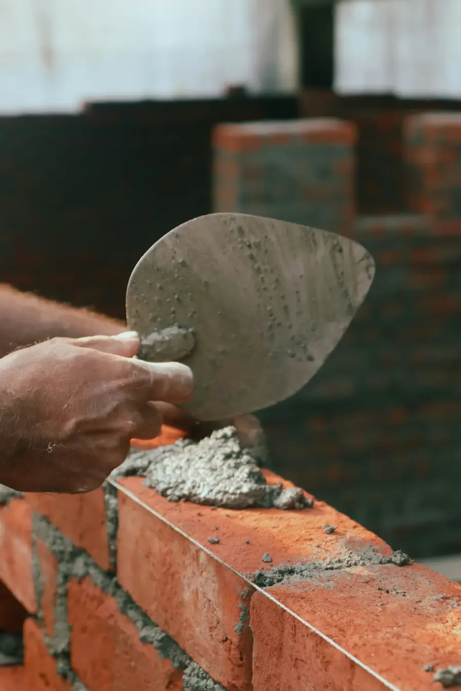 Main d'artisan tenant une truelle de maçonnerie avec du mortier gris frais, en train de rejointoyer un mur de briques