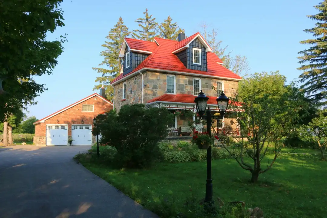 Stone heritage house with red metal roof, wraparound porch and manicured garden, Quebec architectural landmark