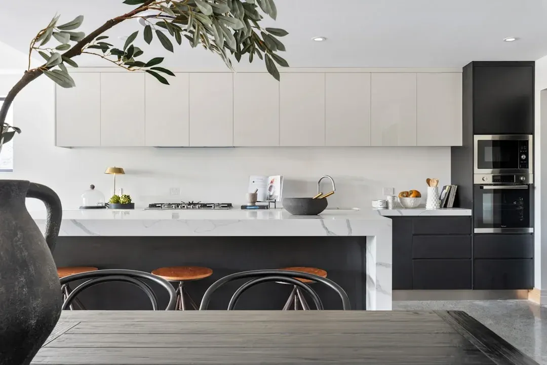 Two-tone kitchen with marble countertop, copper stools, and handleless cabinets