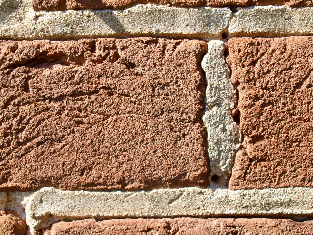 Close-up of old red clay bricks with wide, textured mortar joints, historic lime-mortar masonry