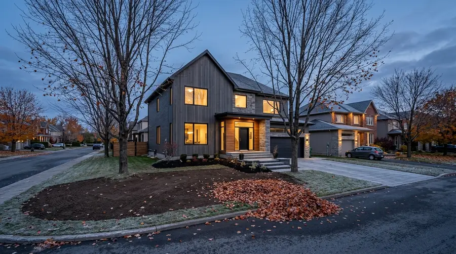 Contemporary Quebec home in late autumn, raked leaves, lit windows at dusk, light frost on the lawn