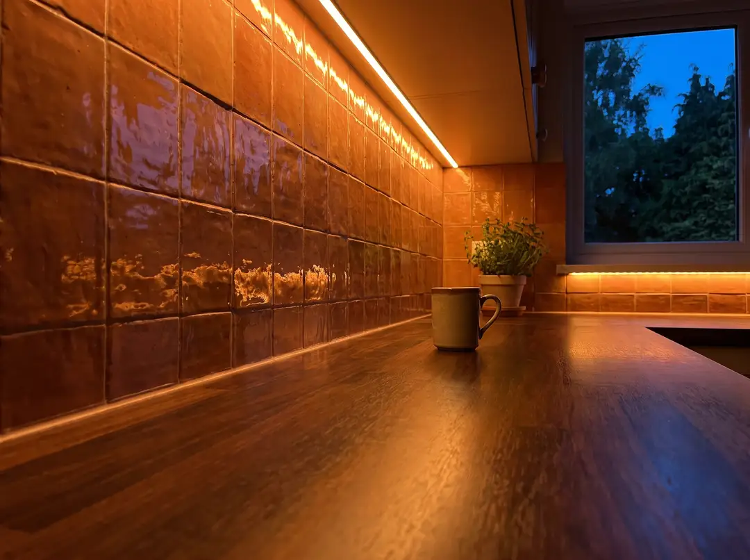 LED under-cabinet lighting washing a terracotta ceramic backsplash and wood countertop in the evening