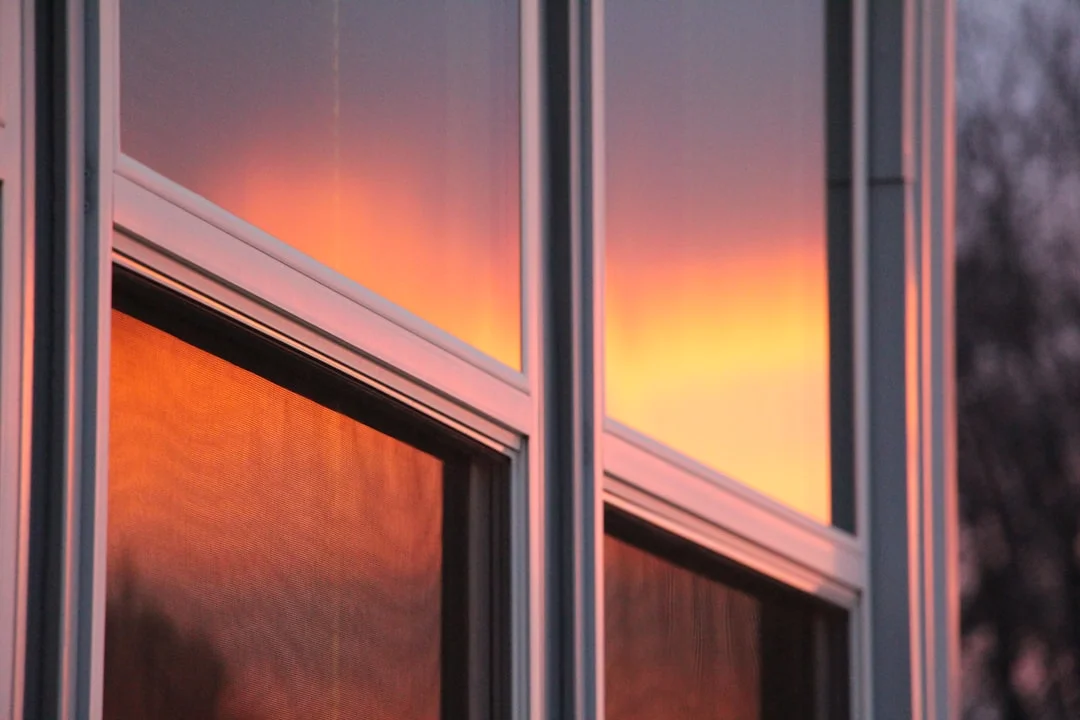 Close-up of white window frames reflecting a vibrant orange and pink sunset