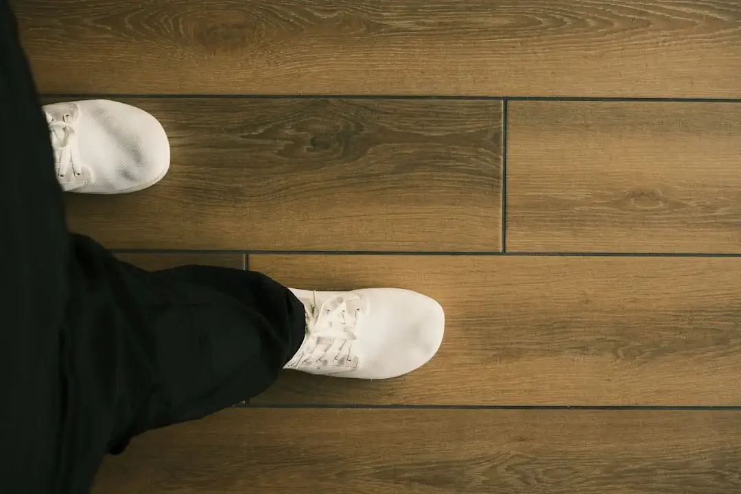 White sneakers standing on wide-plank brown hardwood-style flooring viewed from above