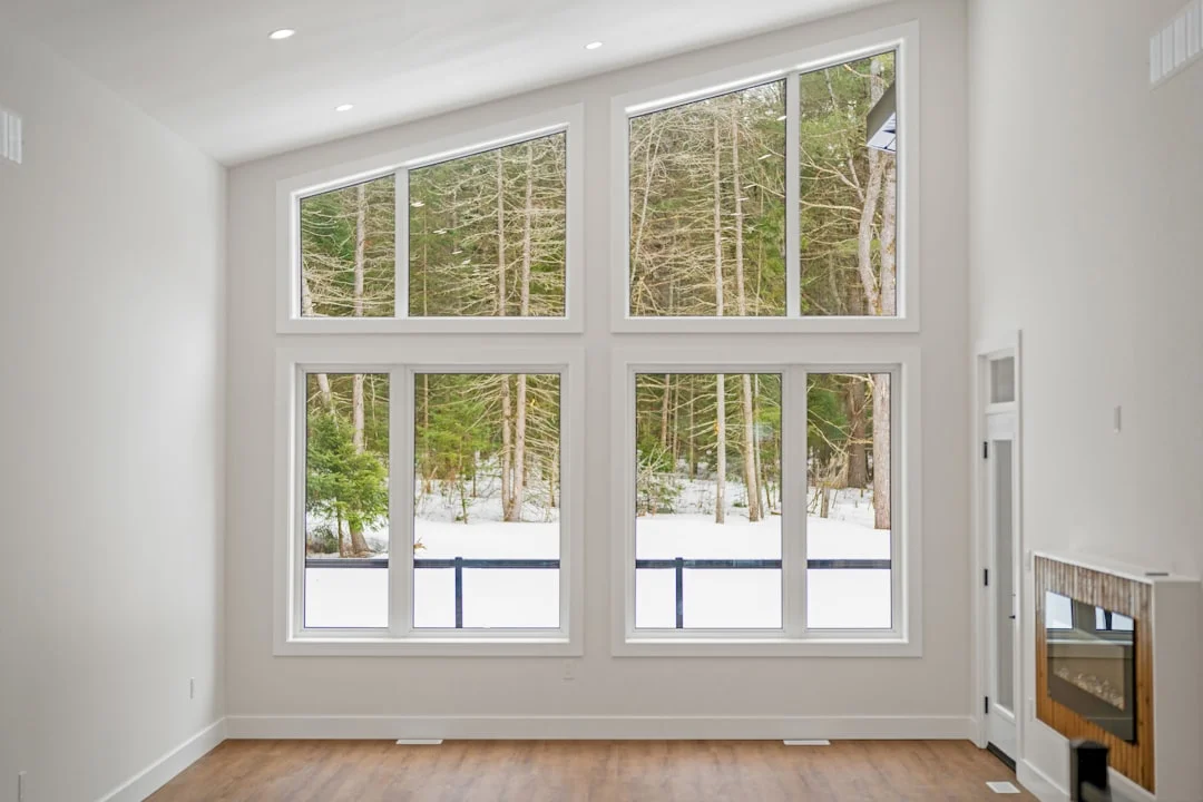 Modern living room with large white-framed windows overlooking a snowy forest